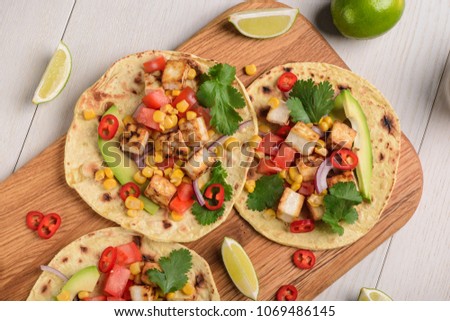 Tortillas with vegan taco filling on wooden cutting board. Tasty blend of avocado, pepper, tomato, corn, cilantro and tofu.