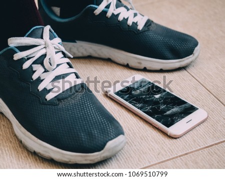 Broken screen smartphone on the tile floor with shoes.