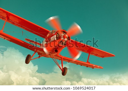 Red biplane flying in the cloudy sky. Retro style Royalty-Free Stock Photo #1069524017