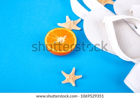 Summer beach bag with white flip flops, sunglasses, seashells, orange fruit on blue background. Flat lay. Top view. Copy space.