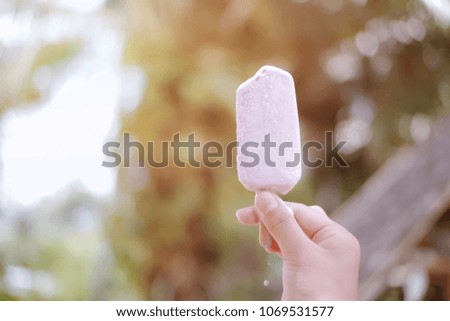 Woman's hands holding melting ice cream on bokeh light nature background