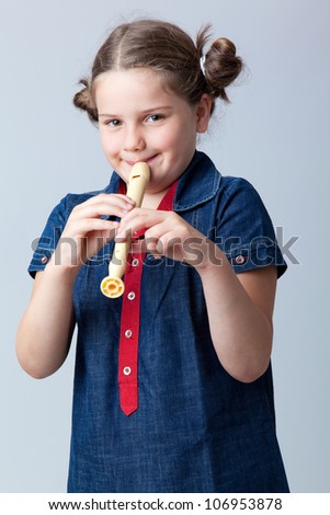 Little girl plays the flute on a grey background