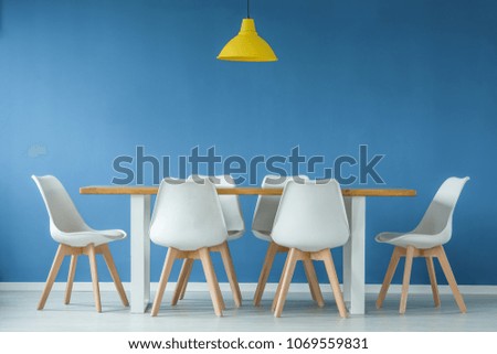 Modern, white and wooden chairs around a dining table and yellow lamp against blue background wall in a minimal style interior