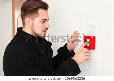 Young man pushing button of fire alarm system, indoors