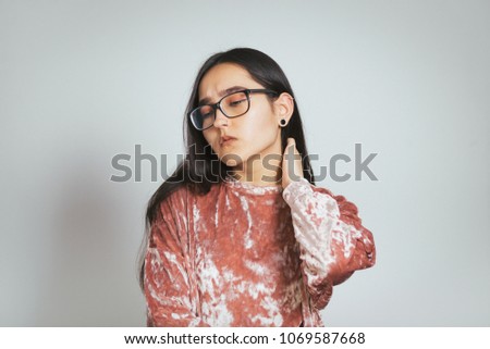 beautiful asian woman has neck pain, wears glasses and pink sweater, studio photo on background