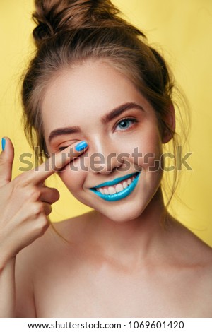 beauty art portrait of white young smiling girl model in punchy pastel tones. blue caramel makeup with nail polish and lipstick on yellow background. Vertical photo Royalty-Free Stock Photo #1069601420