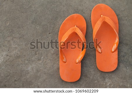A pair of orange flip-flops on cement ground showing concept of couple, holiday, or casual time