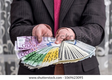Businessman in suit showing and offering euro and dollar notes