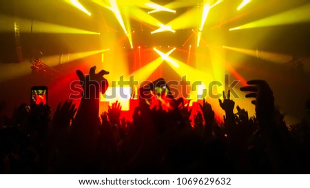 Happy people dance in nightclub party concert and listen to music from DJ on the stage in background. Cheerful crowd celebrate Christmas and New Year party 2019. Young people lifestyle and nightlife.