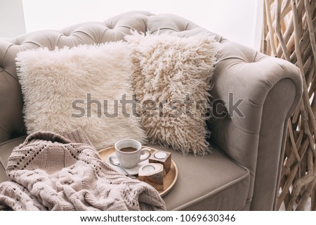 Still life details of nordic living room. Coffee and sweater on the sofa with fur cushions. Cozy winter scene in Scandinavian interior. Royalty-Free Stock Photo #1069630346