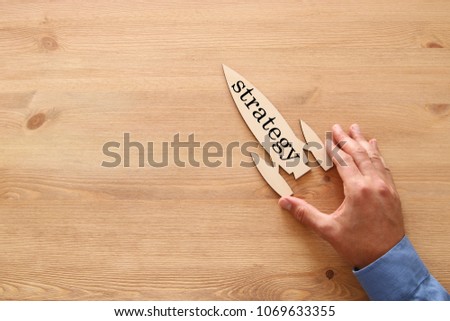 man's hand holding rocket with word - strategy - over wooden background