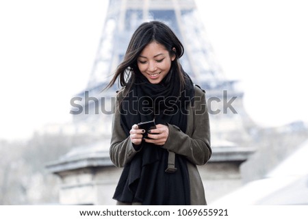 Shot of smiling asian young woman using her mobile phone in front of Eiffel tower.