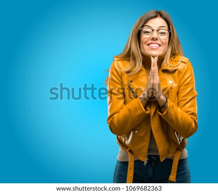 Beautiful young woman with hands together in praying gesture, expressing hope and please concept, blue background