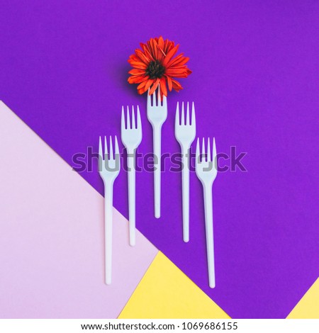 Plastic forks with orange flower on yellow and  purple background of paper textures. Minimal flat lay. surreal food concept of meal