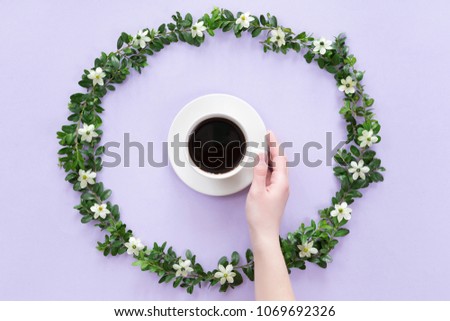 View from above of woman hands with morning cup of tea or coffee in round flowers frame on lilac background, Flat lay style.