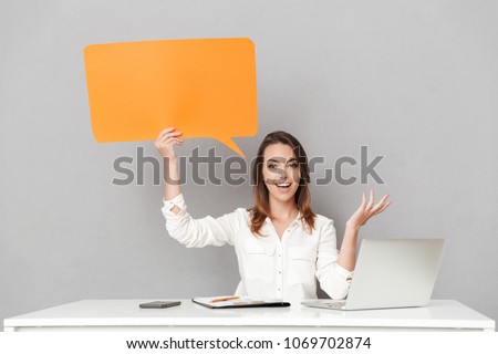 Image of an amazing happy young business woman sitting isolated over grey wall background using laptop computer holding speech bubble.
