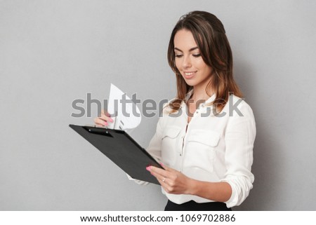 Image of an amazing cheerful young business woman standing isolated over grey wall background holding clipboard.