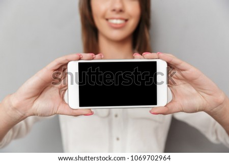 Cropped image of cheerful young business woman standing isolated over grey wall background showing display of mobile phone.