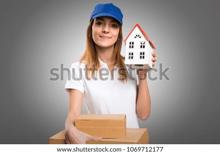 Delivery woman holding a little house on grey background