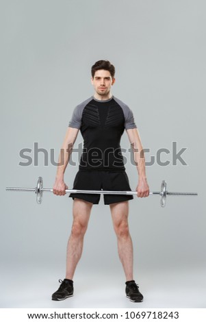 Full length portrait of a concentrated young sportsman lifting heavy barbell isolated over gray background