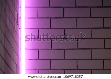 Purple neon fluorescent lamp installed vertically at the corner of brick walls
