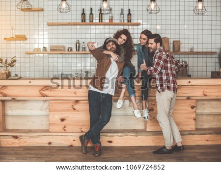 Happy loving couple is making selfie on smartphone and embracing. Their friends are posing and smiling near them. Double date concept