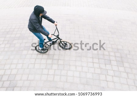 A young man in casual clothing, riding a bike on the rear wheel of a BMX. The minimalist photo of the BMX cyclist is from above. bmx culture