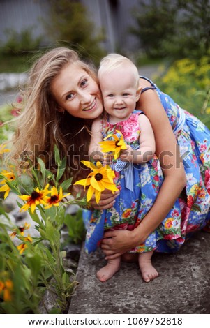 Family. Portrait of beautiful cheerful mother with her cute daugher having fun together in the garden. Smiling girl with yellow flowers