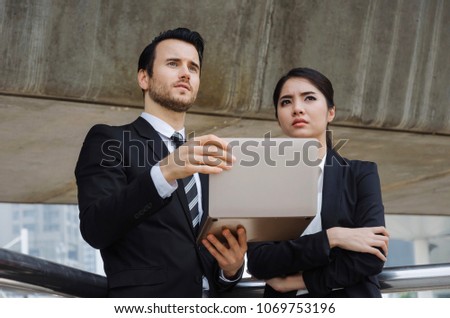 two business people in suit talking and reading information about finance news in laptop computer together standing in modern city, investment, network technology, internet and teamwork concept