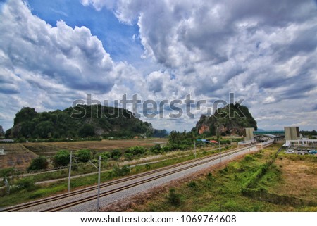 Great landscape view with train railtracks and station as foreground and beautiful mountains and clouds as background.