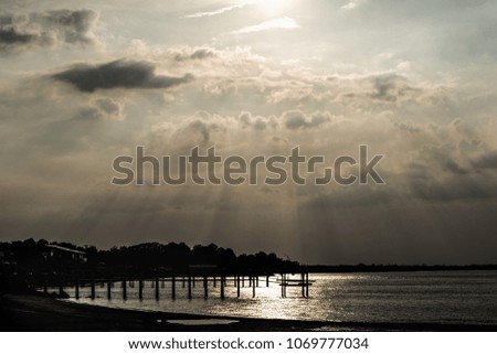Cloudy sunset in the bay with light rays from the sun and silhouette of a shore line. 