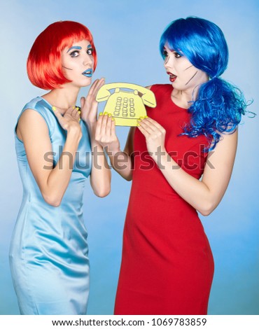 Portrait of young women in comic pop art make-up style. Females in red and blue wigs and dresses call on the phone
