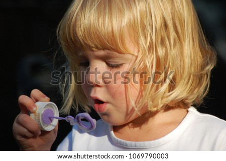 Little blond toddler girl is blowing bubbles.