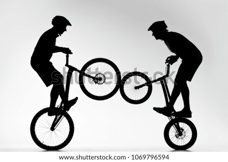silhouettes of trial bikers performing stunt synchronously on white
