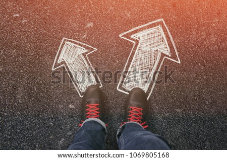 Sneakers on the asphalt road with drawn arrows pointing in two directions. Making decisions and making choices concept. Royalty-Free Stock Photo #1069805168