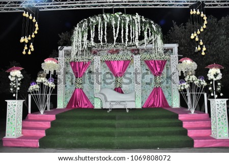 The stage is set for the wedding ceremony in the Oriental style, with crimson curtains, bouquets of white roses, pink umbrellas and green artificial turf under the grass and white sofa in the middle  Royalty-Free Stock Photo #1069808072
