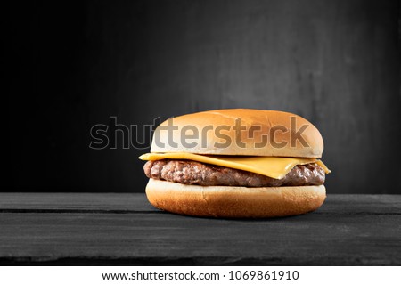 Plain beef burger with cheese on wooden table isolated on black background. Royalty-Free Stock Photo #1069861910