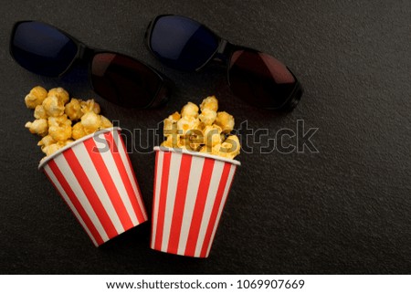 Popcorn in a red and white stripes paper cup on a dark textured background. Top view or flat lay. Entertainment or movie time concept.