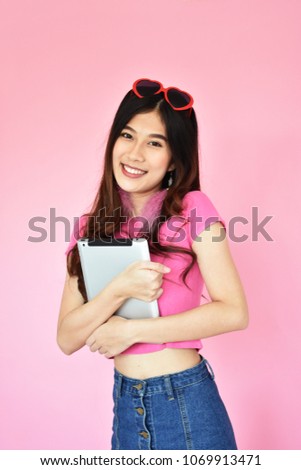Portrait beautiful asian girl holding and using her tablet on pink background, Caucasian model
