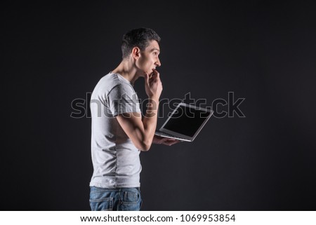 Thoughtful look. Intelligent nice thoughtful man holding a laptop and biting his finger while looking for new ideas