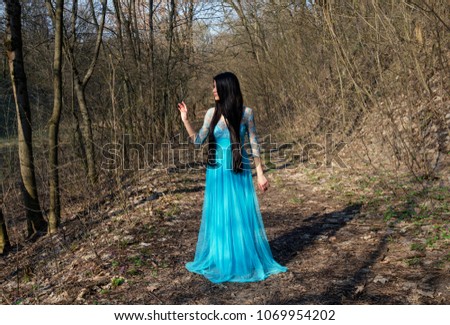 girl with long and beautiful hair in blue length dress against a forest background, spring warm day