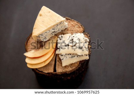 cheese dor blu on a wooden stand on a dark background, a piece entirely and cut into pieces