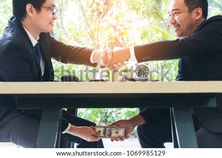 Tricky businessman shaking hand to make agreement and taking bribe corruption under table. Entrepreneur passing cash money under table to his corrupted partner. Business bribery corruption concept. Royalty-Free Stock Photo #1069985129