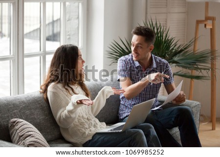 Young couple arguing about high domestic bills to pay with laptop and documents, unhappy family having conflict disagreement discussing unpaid debt or money problems sitting together on sofa at home Royalty-Free Stock Photo #1069985252