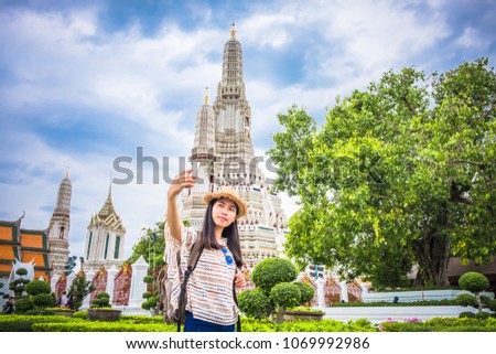 Asian woman tourist with backpack is taking a photo or selfie with smartphone during a travel and relax in holiday at pagoda arun temple It is a landmark and attractions of Bangkok Thailand.