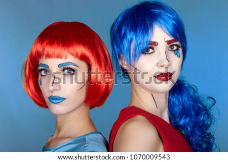 Portrait of young women in comic pop art make-up style. Females in red and blue wigs on blue background.