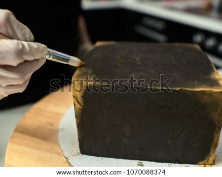 Step-by-step preparation of black designer cake. The confectioner decorates a black cake, gold food paint.