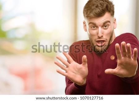 Handsome young man disgusted and angry, keeping hands in stop gesture, as a defense, shouting