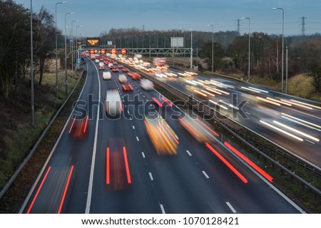 Fast moving traffic drives along the M42 in Warwickshire during evening rush hour, leaving traffic light trails as the vehicles are controlled using Active Traffic Management for each motorway lane Royalty-Free Stock Photo #1070128421
