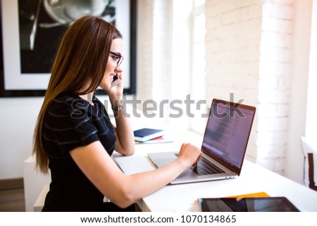 Happy business woman talking via cellphone with partner and reading financial information form laptop computer.Smiling female skilled editor calling via cellphone and searching information on notebook